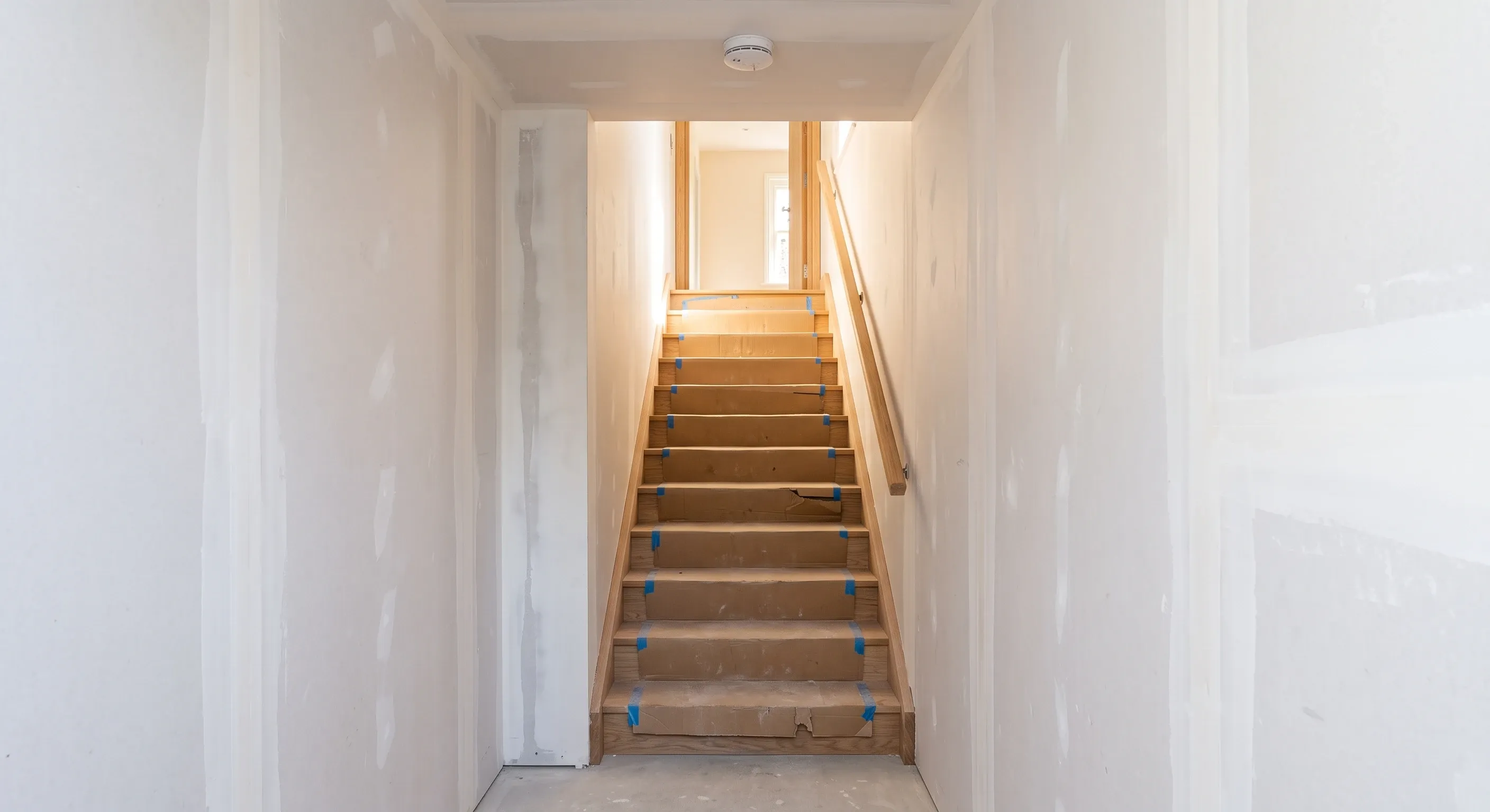 A boarded basement escape stair rising toward daylight from the hall above.