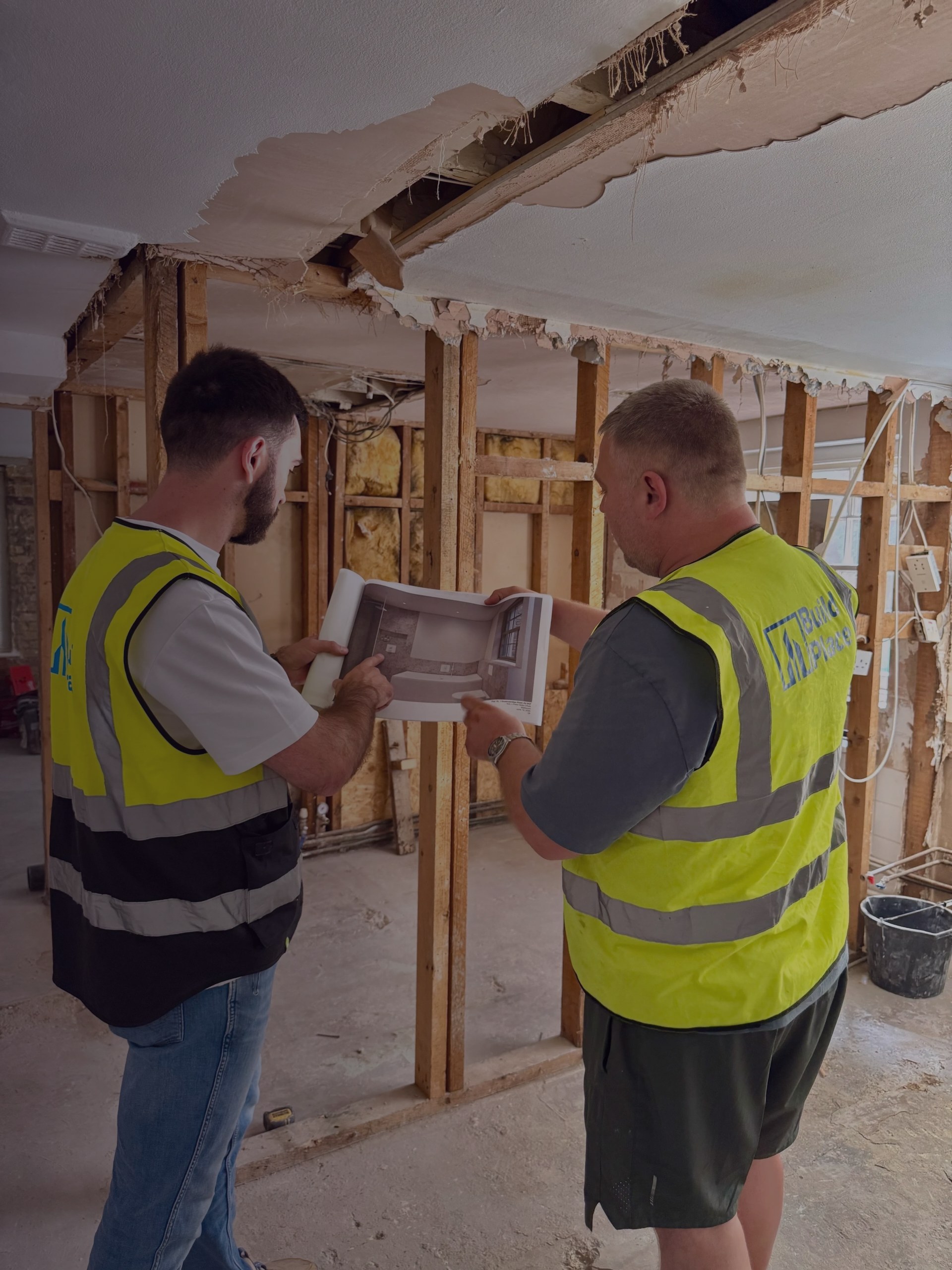 Builders in high-visibility jackets looking over plans inside a house being renovated.