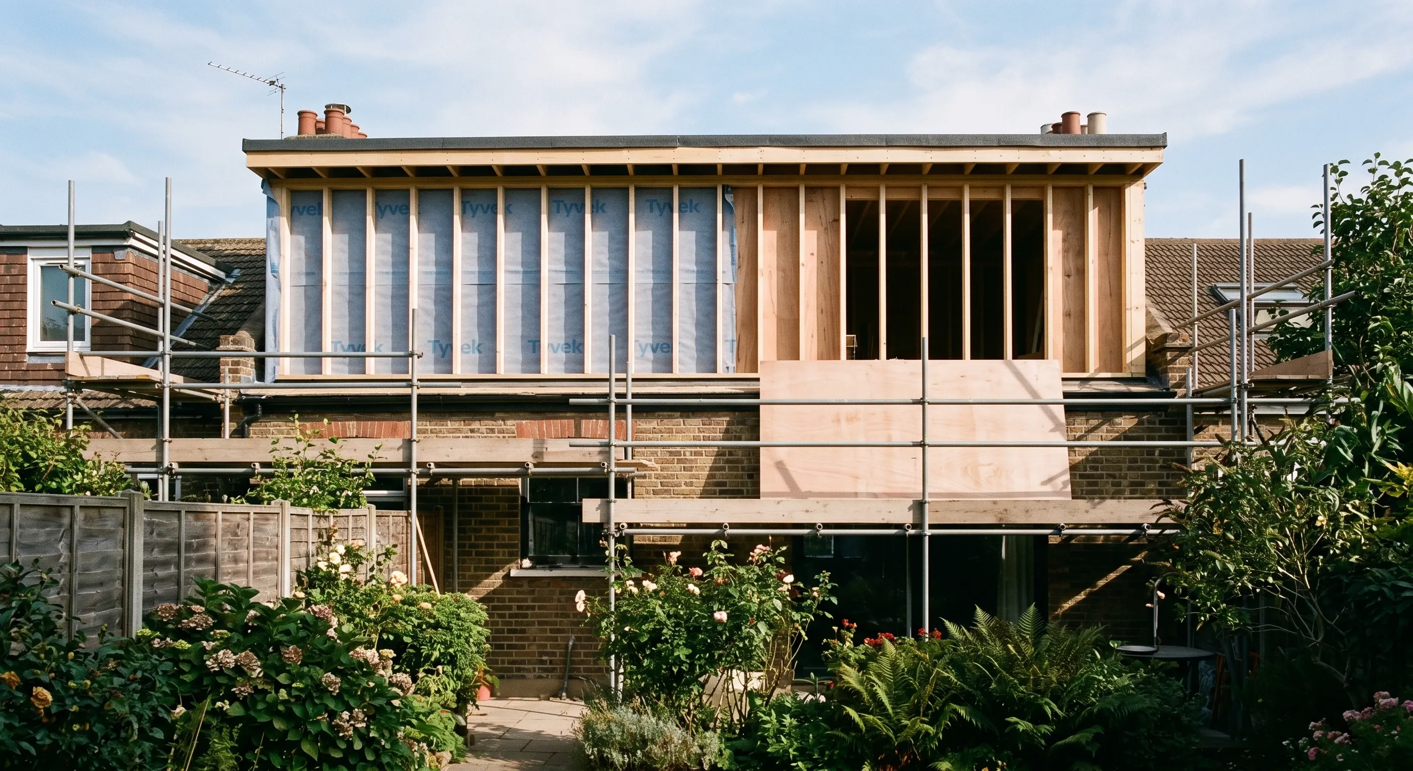 A rear dormer under construction in timber frame, seen from the garden with scaffolding still up.