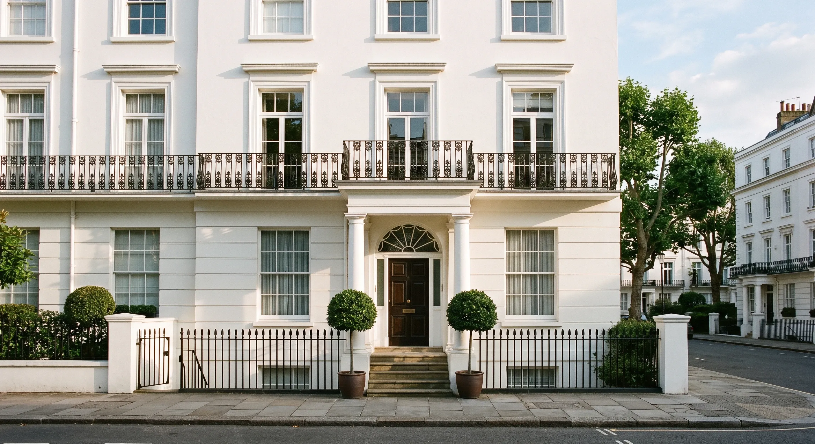 A white stucco terraced house with a columned porch and wrought iron balcony.