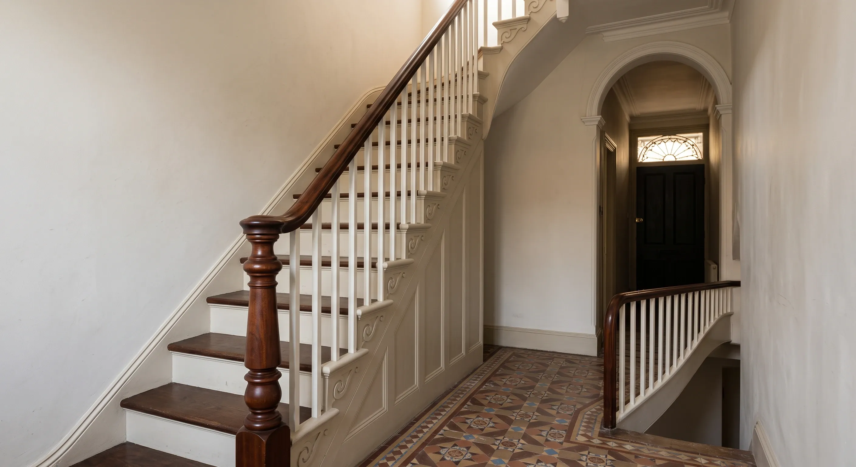 A Victorian terrace entrance hall with a cut string stair rising to a half landing, turned newel, slender balusters and encaustic floor tiles.