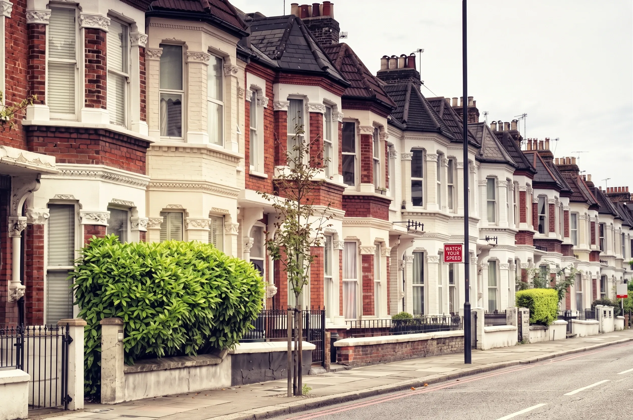 A row of Victorian terraced houses in Wandsworth with bay windows and white stucco detailing, and a black cab passing in motion blur.