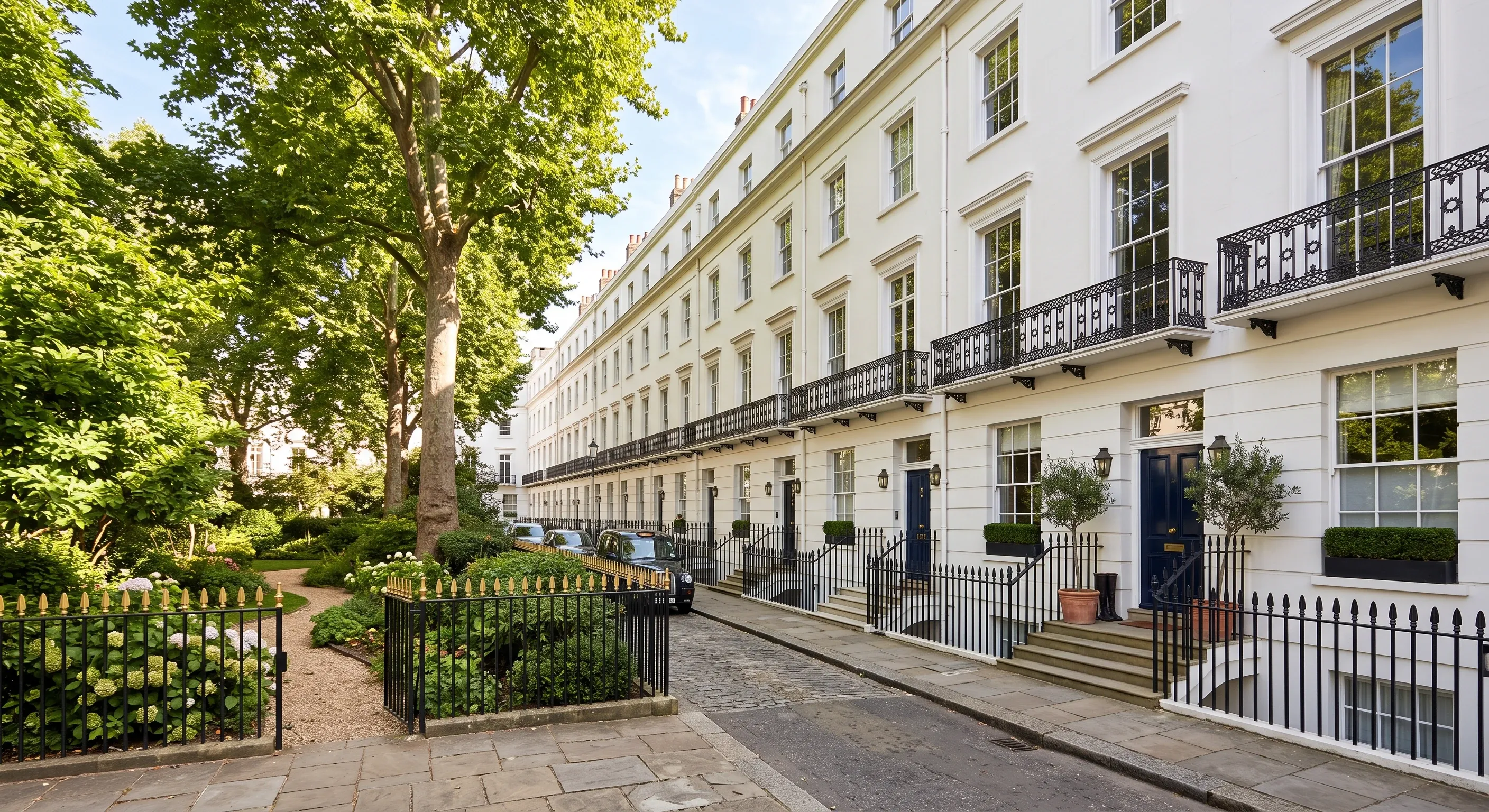A row of white stucco townhouses with black railings beside a private garden square.