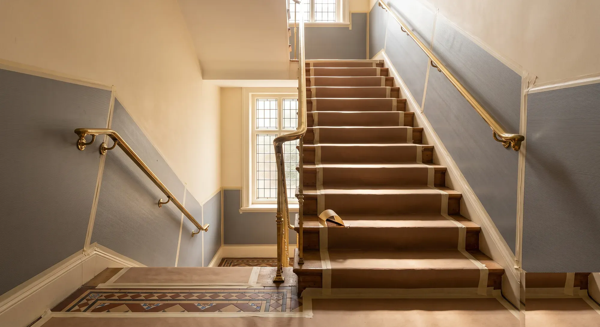 A communal stairwell with paper protection taped over the treads and brass handrails either side.