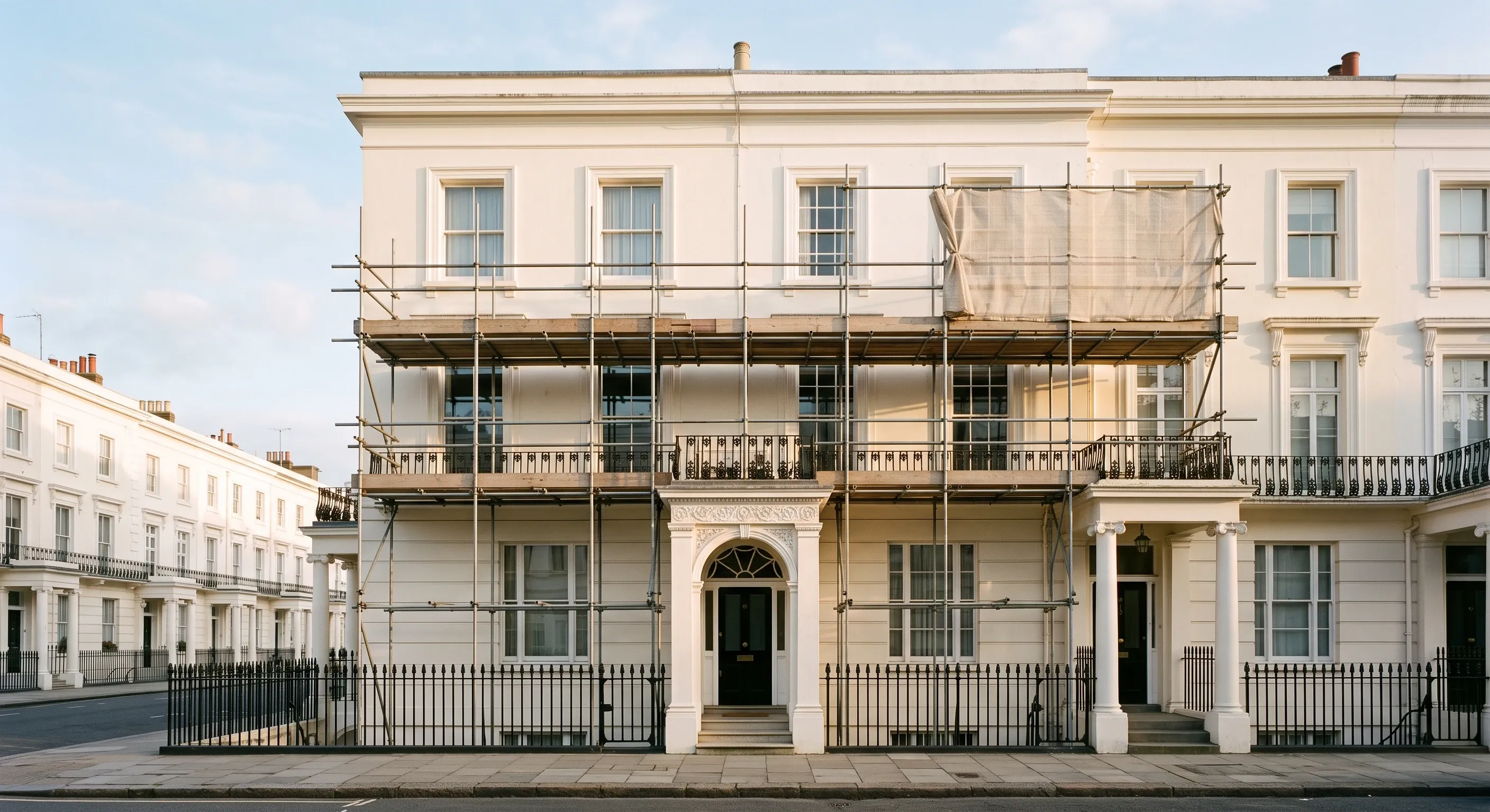 Scaffolding against the stucco front of a white London terrace on a quiet morning.